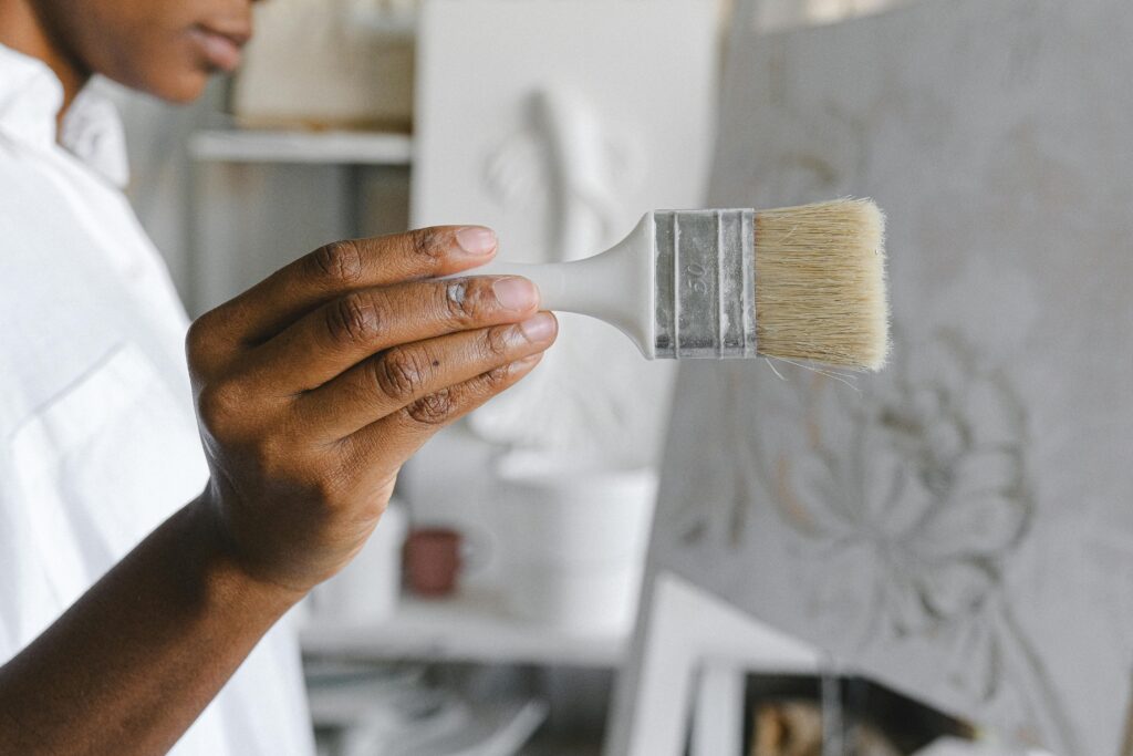 Detailed view of an artist's hand holding a paintbrush in a studio setting, focusing on creative work.